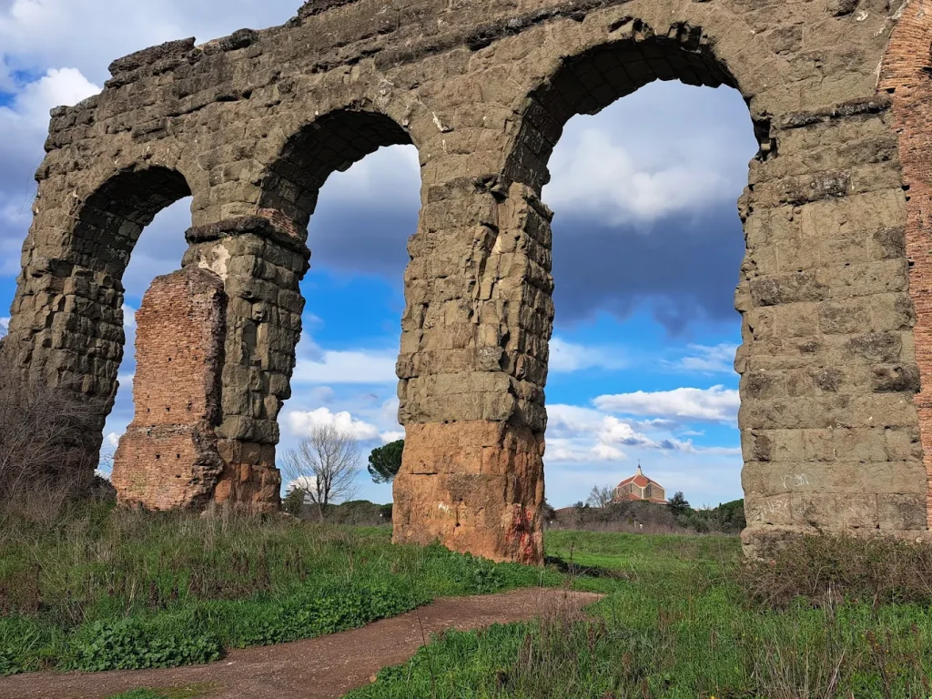 Ancient Roman aqueduct arches at Parco degli Acquedotti in Rome under a bright blue sky